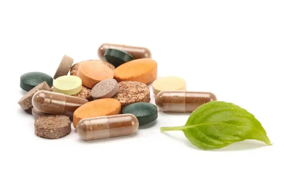 A pile of vitamin and supplement tablets and capsules beside a fresh green leaf